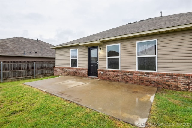 rear view of property featuring a patio, a shingled roof, a lawn, fence, and brick siding