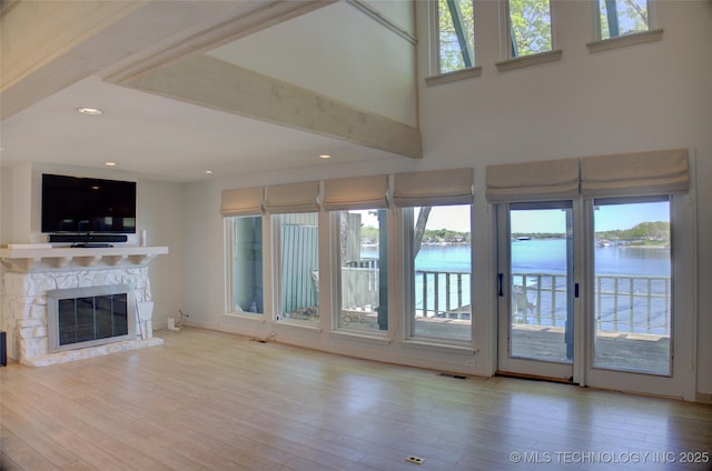 unfurnished living room featuring recessed lighting, a water view, a stone fireplace, visible vents, and wood finished floors