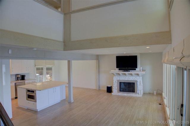 unfurnished living room with a stone fireplace, light wood finished floors, and a towering ceiling