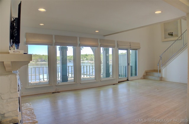 unfurnished living room featuring recessed lighting, stairs, a water view, and wood finished floors