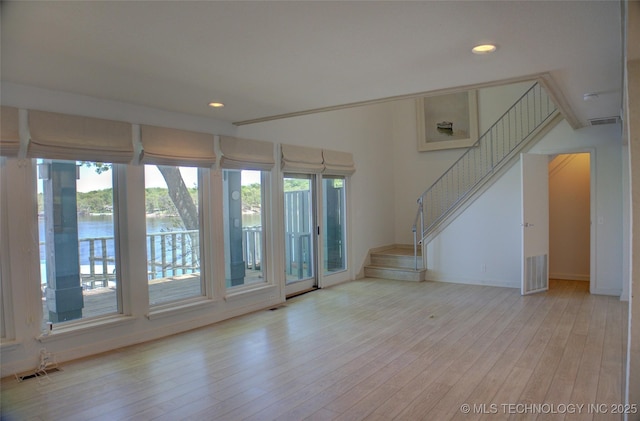 unfurnished living room with recessed lighting, stairway, a water view, visible vents, and wood finished floors
