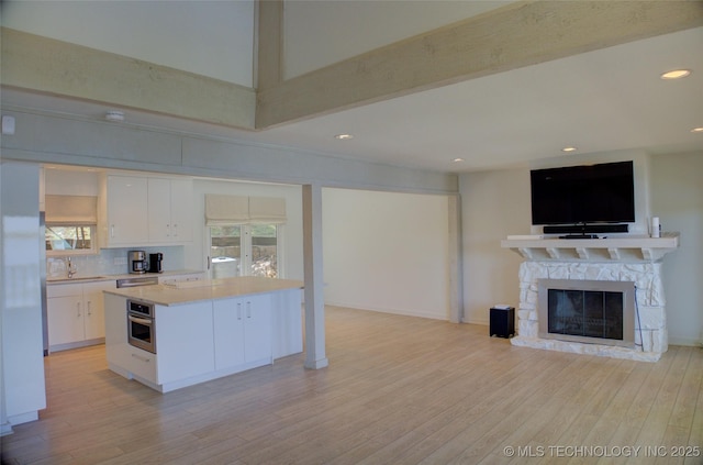 kitchen featuring oven, backsplash, light countertops, white cabinets, and open floor plan