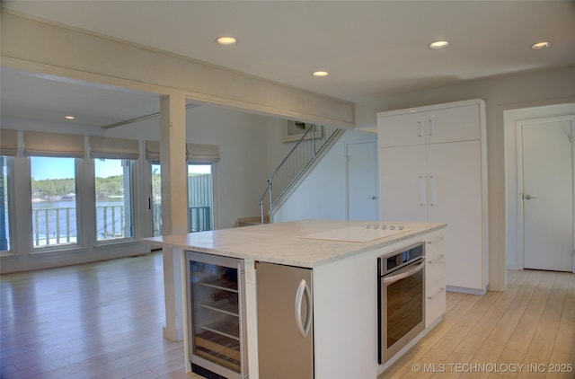 kitchen with stainless steel appliances, open shelves, white cabinets, light wood-type flooring, and wine cooler