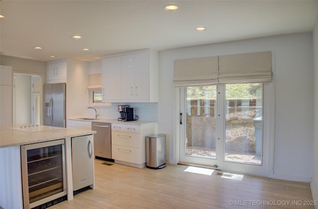 kitchen featuring a sink, appliances with stainless steel finishes, beverage cooler, light wood-type flooring, and recessed lighting