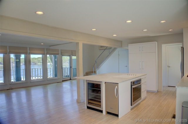 kitchen with white cabinets, fridge, light wood-style floors, wine cooler, and stainless steel oven