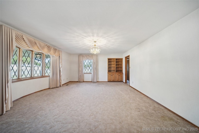 601 N Okmulgee Ave, Okmulgee, OK 74447 - carpeted empty room with built in shelves, a notable chandelier, and baseboards