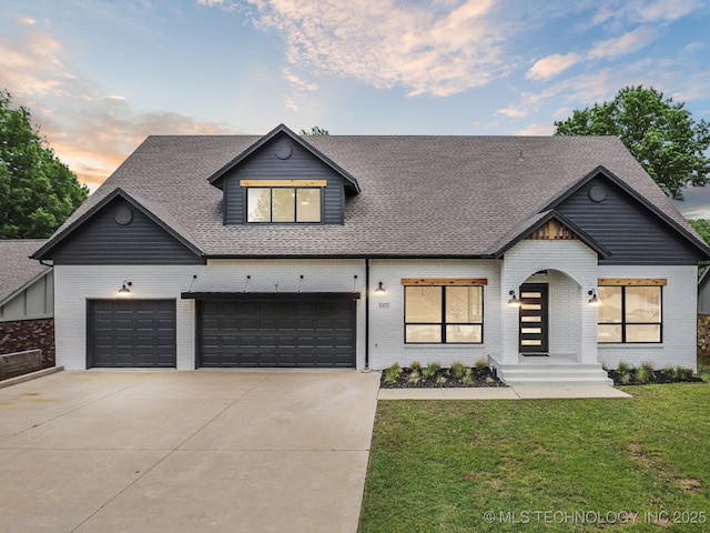 modern farmhouse with driveway, a shingled roof, a front yard, an attached garage, and brick siding