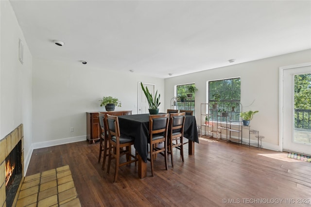 dining area with dark wood-type flooring, visible vents, a warm lit fireplace, and baseboards
