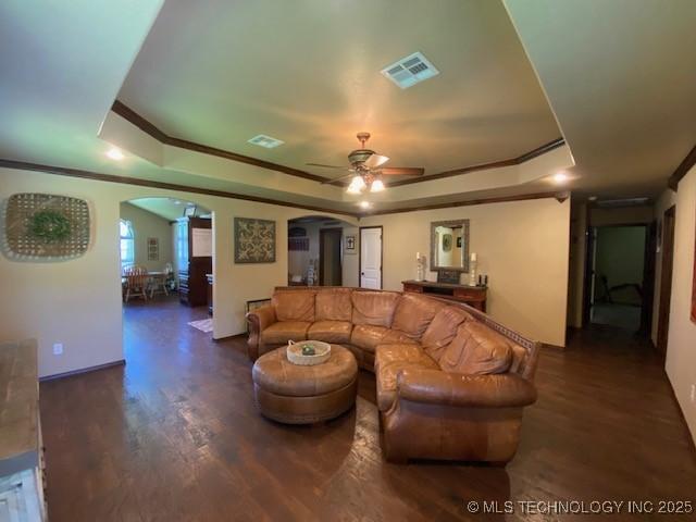 living area featuring visible vents, arched walkways, a ceiling fan, and a tray ceiling