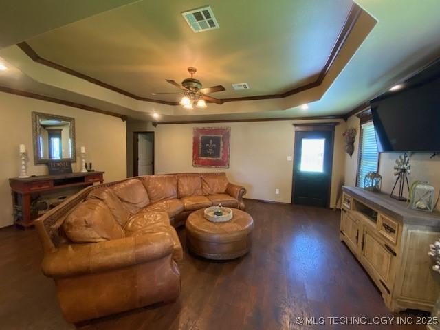 living room featuring ceiling fan, a tray ceiling, crown molding, visible vents, and dark wood finished floors