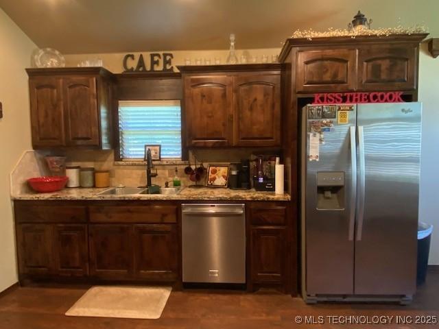 kitchen with light stone countertops, stainless steel appliances, dark brown cabinets, and a sink