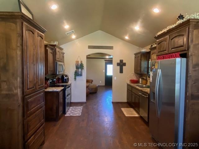 kitchen with dark wood-style floors, stainless steel appliances, visible vents, vaulted ceiling, and arched walkways