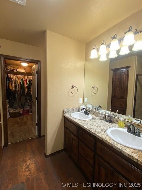 full bathroom with a spacious closet, wood finished floors, double vanity, and a sink