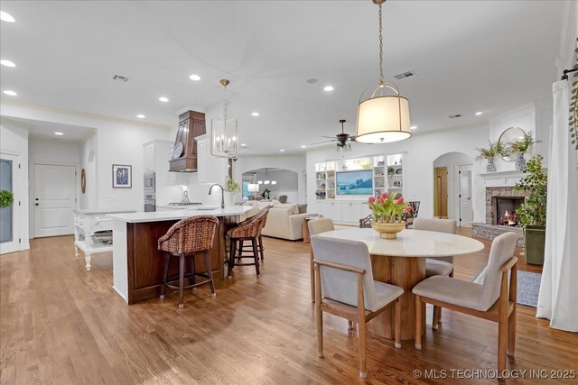 dining space with recessed lighting, ceiling fan, a stone fireplace, visible vents, and arched walkways