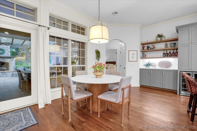dining area with beverage cooler, wood finished floors, arched walkways, ornamental molding, and visible vents