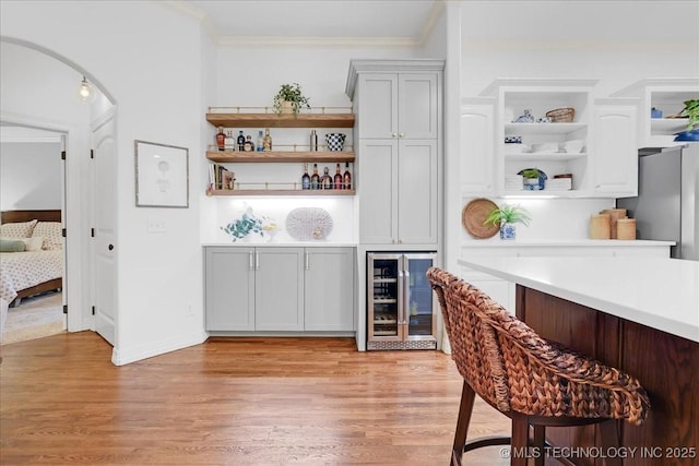 bar featuring ornamental molding, wine cooler, a dry bar, and light wood-style floors