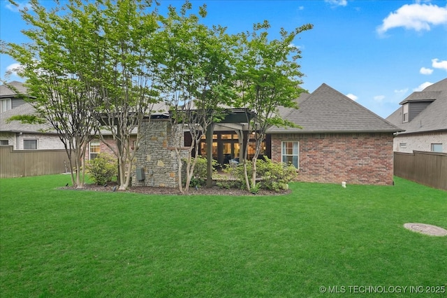 back of house with fence, a yard, a shingled roof, and brick siding