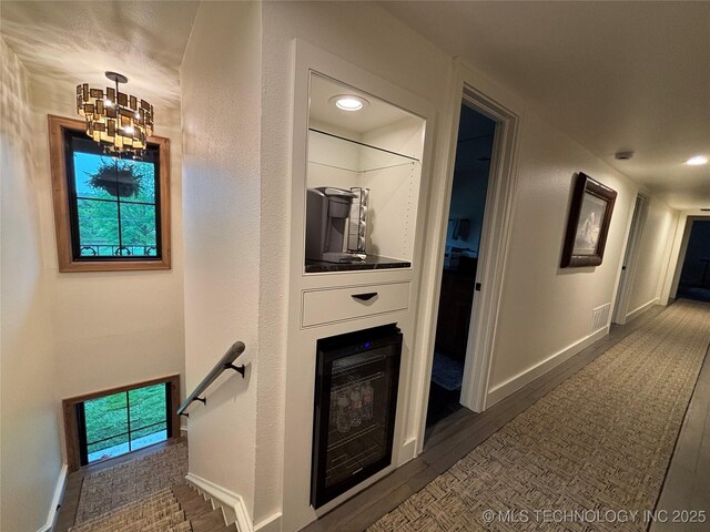 hallway featuring wood finished floors, an upstairs landing, baseboards, visible vents, and a notable chandelier