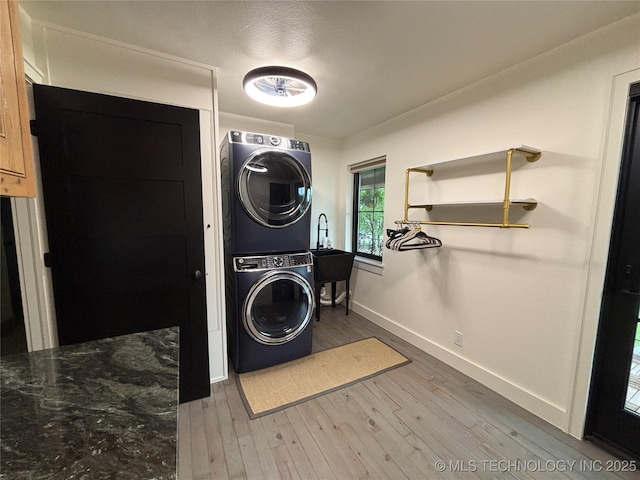 washroom with stacked washer / dryer, light wood-style flooring, laundry area, and baseboards
