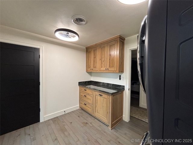 kitchen featuring dark countertops, light wood finished floors, visible vents, and freestanding refrigerator