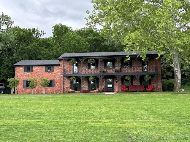 view of front of home featuring a front yard, brick siding, covered porch, and a balcony