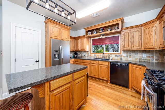 kitchen featuring appliances with stainless steel finishes, a sink, light wood-style floors, backsplash, and dark countertops