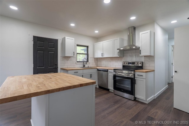 kitchen featuring white cabinets, wood counters, wall chimney exhaust hood, stainless steel appliances, and dark wood-type flooring