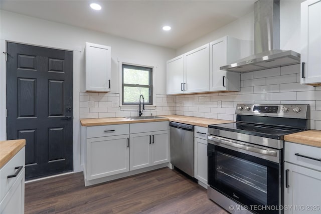 kitchen featuring butcher block countertops, a sink, wall chimney range hood, and stainless steel appliances