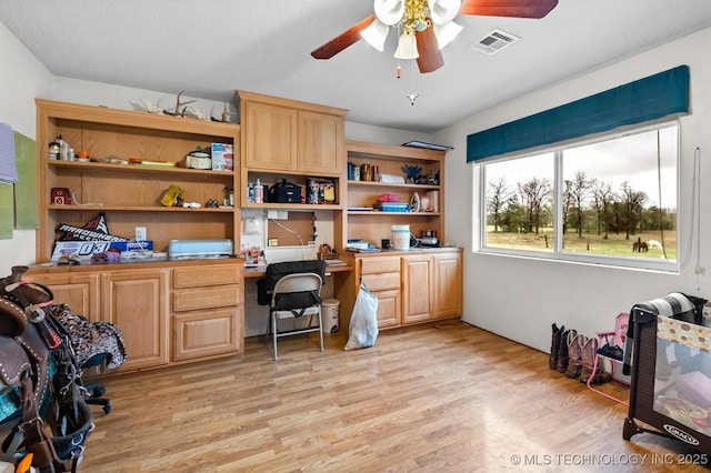 home office featuring light wood-style floors, visible vents, a ceiling fan, and built in study area