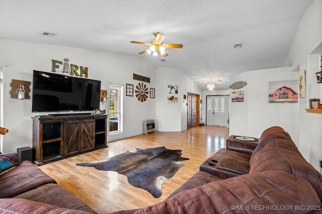 living area featuring light wood-style floors, heating unit, a ceiling fan, visible vents, and lofted ceiling