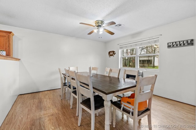 dining area featuring a textured ceiling, visible vents, a ceiling fan, and light wood-style floors