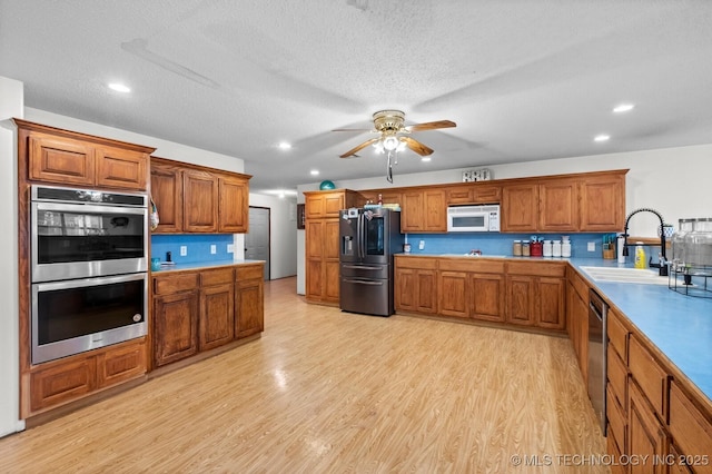 kitchen featuring a sink, appliances with stainless steel finishes, light wood-style floors, ceiling fan, and brown cabinetry