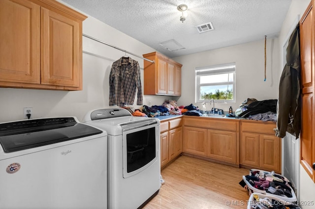 clothes washing area with a textured ceiling, independent washer and dryer, a sink, light wood finished floors, and cabinet space
