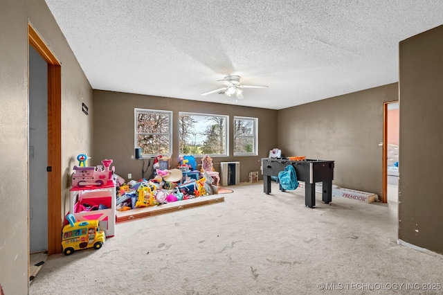 recreation room with ceiling fan, a textured ceiling, and carpet