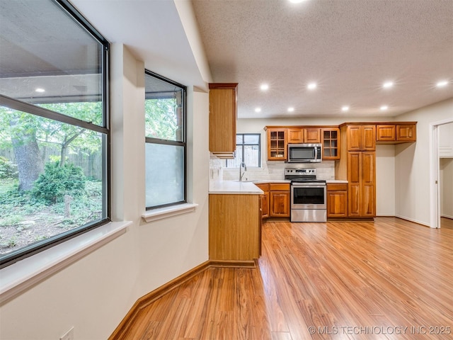 kitchen with a sink, brown cabinetry, light wood-type flooring, light countertops, and appliances with stainless steel finishes