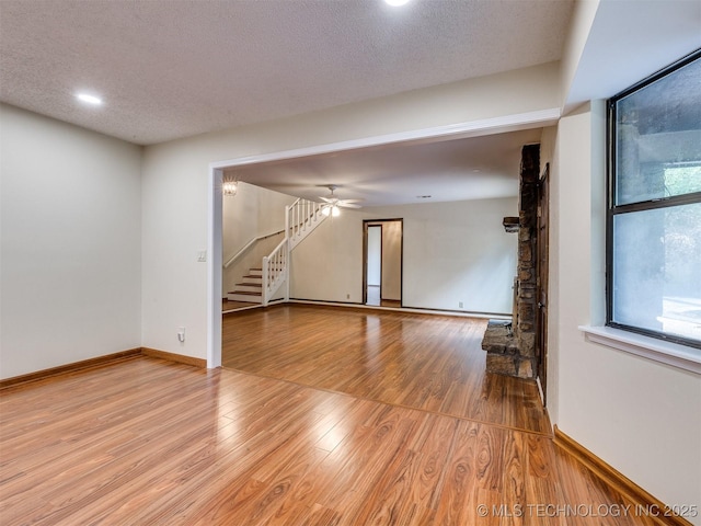 unfurnished living room featuring baseboards, a textured ceiling, stairway, and light wood-type flooring