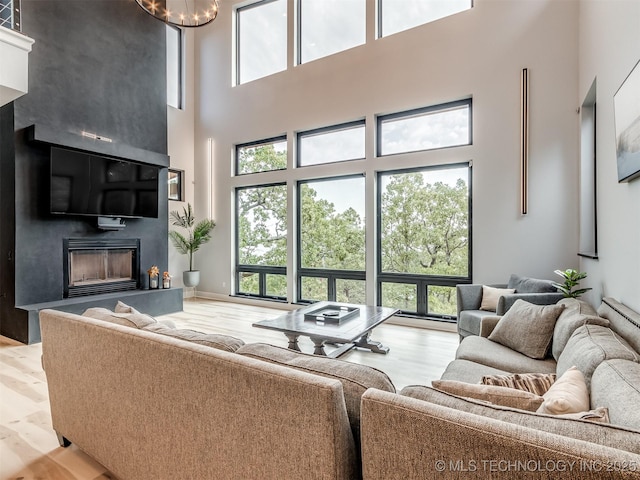 living area with a large fireplace, light wood finished floors, and a towering ceiling
