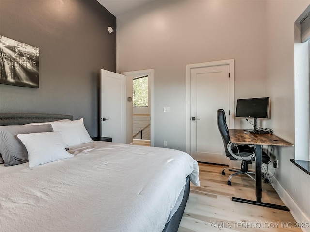 bedroom featuring baseboards, light wood-type flooring, and a high ceiling