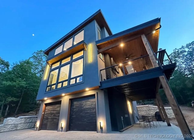 exterior space with a ceiling fan, stucco siding, a balcony, and an attached garage