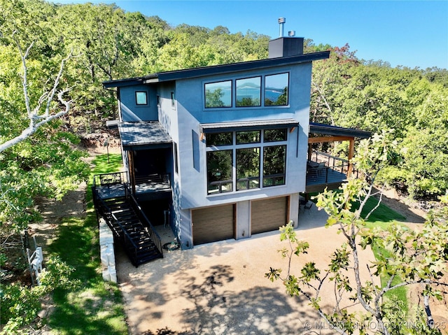 view of front of home featuring a wooded view, a chimney, stucco siding, stairway, and a garage