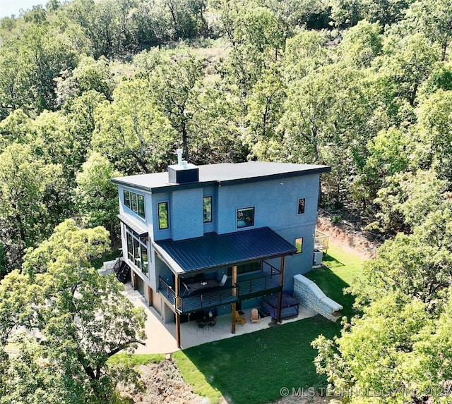 exterior space featuring stucco siding, a yard, a patio, and a forest view
