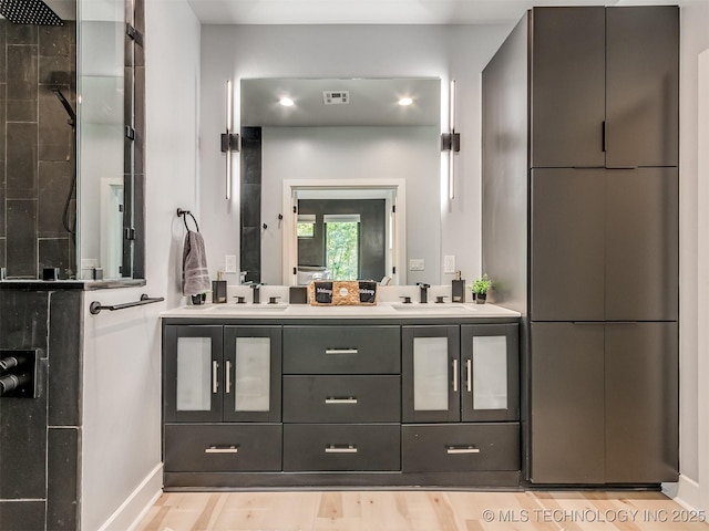 full bath with baseboards, a tile shower, double vanity, and a sink