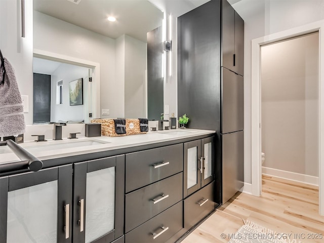 full bath featuring double vanity, wood finished floors, toilet, and a sink