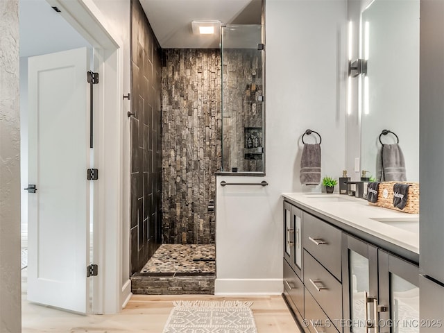 bathroom featuring a sink, double vanity, baseboards, walk in shower, and wood finished floors