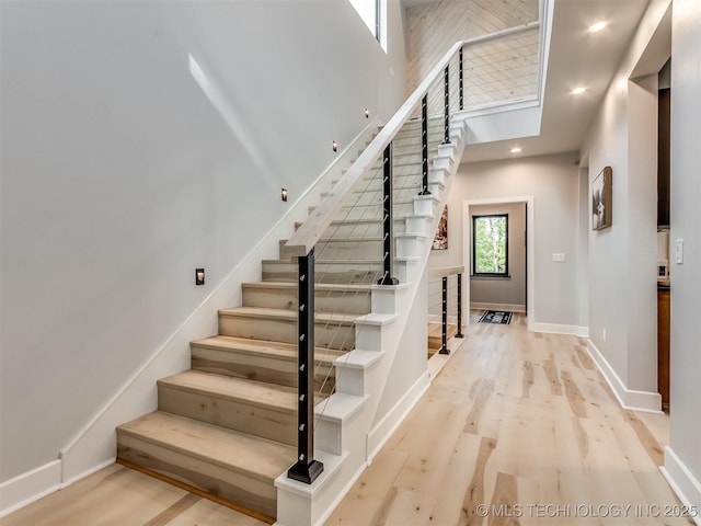 staircase with baseboards, recessed lighting, wood finished floors, and a high ceiling