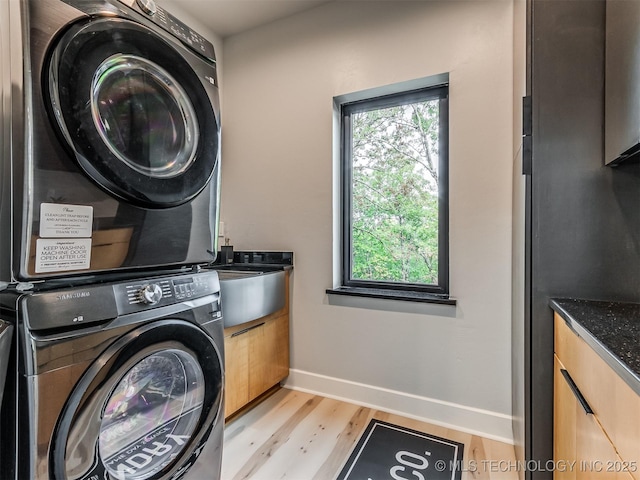 clothes washing area with light wood-style floors, cabinet space, stacked washing maching and dryer, and baseboards