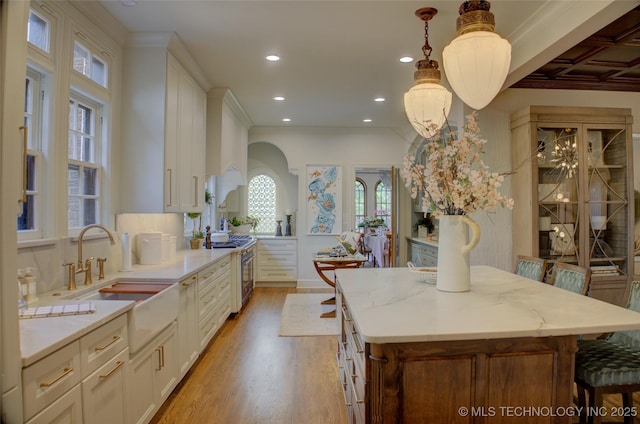 2156 S Owasso Pl, Tulsa, OK 74114 - kitchen featuring stainless steel stove, a center island, arched walkways, a sink, and light wood finished floors