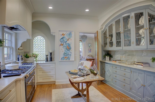 2156 S Owasso Pl, Tulsa, OK 74114 - kitchen featuring crown molding, high end stainless steel range, light wood finished floors, arched walkways, and glass insert cabinets