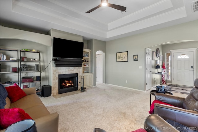 living room with arched walkways, carpet floors, a fireplace, a raised ceiling, and a ceiling fan