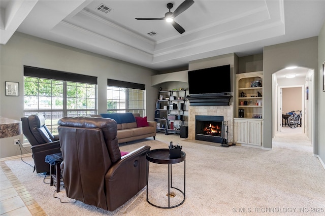living room with a fireplace with flush hearth, a raised ceiling, a ceiling fan, and visible vents